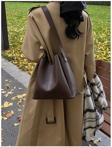 Detailed back view of a dark brown leather bucket bag styled with a trench coat