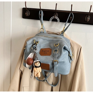 Close-up of light blue versatile bag featuring retro leather patches and bear doll charm