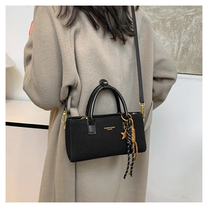 Close-up of black lychee-grain leather crossbody bag with gold hardware and star charm