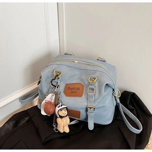 Detail of light blue denim-style bag with plush bear charm and sports accessories