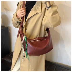 Detail of burgundy crescent bag featuring decorative woven cords and soft leather texture