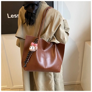 Detail of a brown leather tote bag with a cute plush bear charm on a khaki trench coat
