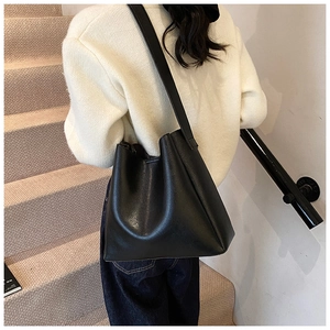 Minimalist black matte leather tote bag with wide shoulder strap shown on a model
