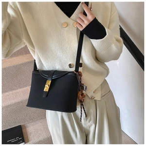 Detail of black bucket bag with gold clasp and donut charm worn by a model in interior