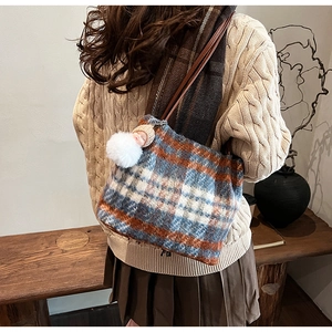 Détail du sac cabas en laine à carreaux avec pompon et breloque sur pull en maille