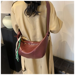 Detail of burgundy crescent bag in litchi grain leather with woven rope pendant