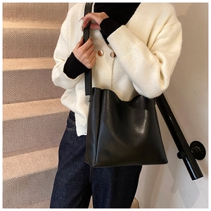 Detail of a black faux leather bucket bag with wavy rim shown on a model indoors