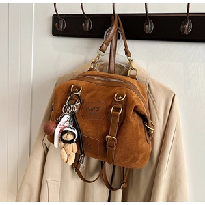 Close-up of brown denim bag with leather trim, metal zippers, and cute bear pendant