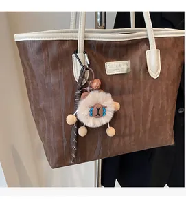 Close-up of brown wavy texture tote bag with cream leather trim and plush sheep charm