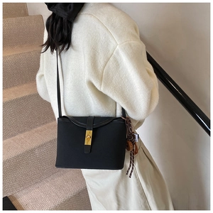 Detail of black crossbody bucket bag with golden twist lock and woven charm pendant
