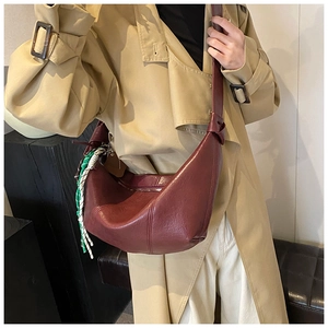 Detail of burgundy half-moon crossbody bag with woven charm on khaki trench coat