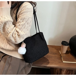 Détail du sac cabas noir texturé avec breloque blanche dans un cadre de vie urbain