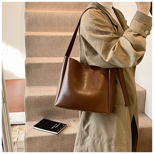 Detail of a deep brown leather bucket bag featuring a wide shoulder strap and matte finish
