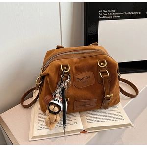 Detail of caramel suede Boston bag with gold hardware and a cute teddy bear charm