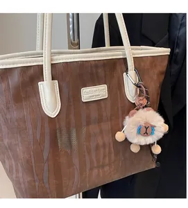 Detail of a brown textured tote bag with cream handles and a cute sheep plush pendant