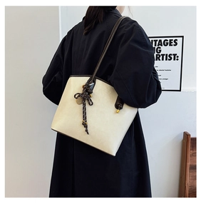 Chic beige tote bag featuring a decorative woven knot charm and stylish brown trim