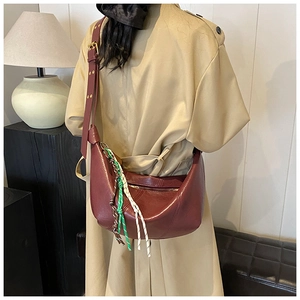 Detailed view of a dark red crescent bag with woven charm and stylish wide shoulder strap