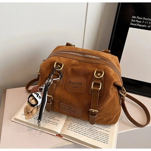 Detail of a brown suede bag with gold zippers and a cute white bear charm accessory