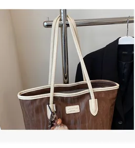 Detail of a brown tote bag featuring contrast cream handles and a plush pompom charm