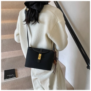 Detail of black matte bucket bag with gold clasp and decorative striped silk scarf