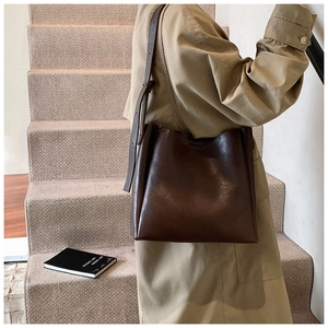 Dark brown leather tote bag with wide strap worn with a khaki trench coat indoors