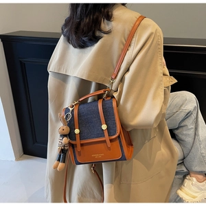 Close-up of contrast color denim shoulder bag with leather straps and a cute bunny charm