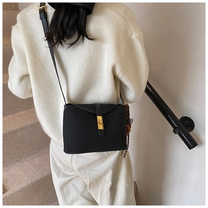 Detail of minimalist black crossbody bag with gold metallic clasp on white sweater outfit