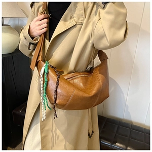 Detail of a brown leather crescent bag featuring a stylish three-color woven rope pendant