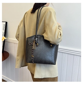 Detailed view of black vintage tote bag with gold badminton racket charm and woven strap