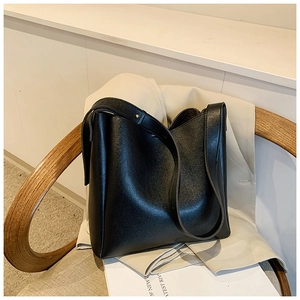Close-up of black leather bucket bag with lychee texture on a wooden chair with a blazer