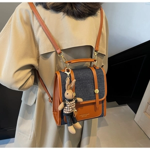 Detail of denim and brown leather patchwork backpack featuring a knitted rabbit charm