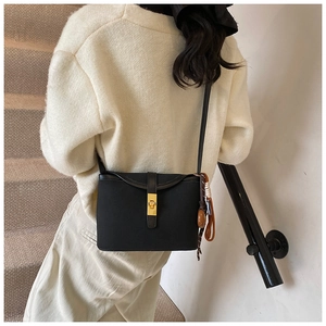 Detail of a matte black crossbody bucket bag with golden buckle and woven charm