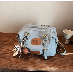 Detail of light blue pebble leather Boston bag with creative charms on wooden desk