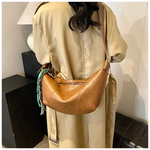 Detail of a brown leather crescent bag with a decorative green and white braided charm