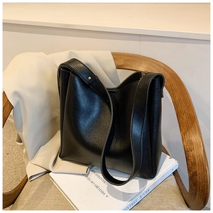 Minimalist black leather tote bag with gold hardware placed on a wooden chair