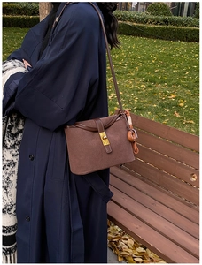 Detailed close-up of brown suede bucket bag featuring a gold clasp and donut-shaped charm