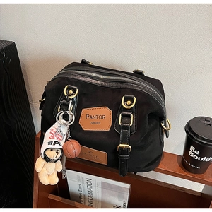 Detail of black nylon tote bag featuring brown leather logo tag and creative bear charm