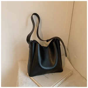 Detail view of a black matte leather bucket bag with a wide strap on a minimalist background