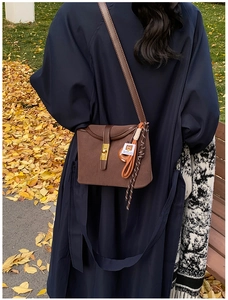 Close-up of brown suede crossbody bucket bag with gold lock and braided rope detail