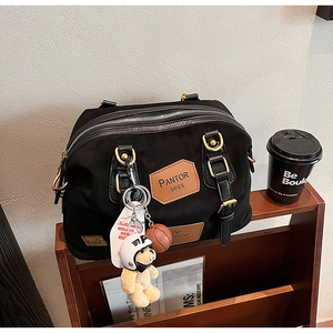 Detail of black canvas bag featuring a brown leather logo and cute teddy bear keychain