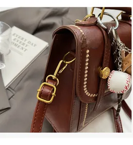 Detail of vintage brown leather bag showing gold wavy stitching and baseball charm