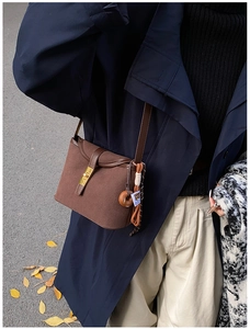 Detail of vintage brown matte bucket bag with gold clasp and tassel on a stylish coat