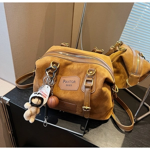 Detail of a brown suede Boston bag with gold hardware, bear charm and mirror reflection