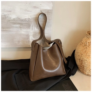 Detail of minimalist dark brown leather bucket bag placed on a black blazer jacket