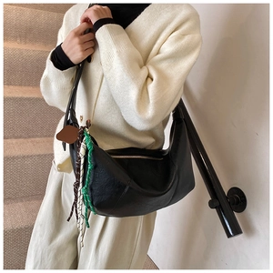 Detail of black crescent hobo bag with braided rope charm worn by a model