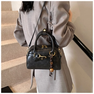 Détail d'un sac Boston en cuir noir avec ferrures dorées porté par un mannequin