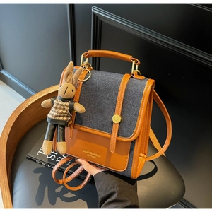 Close-up of contrast denim and brown leather backpack with a plush rabbit charm