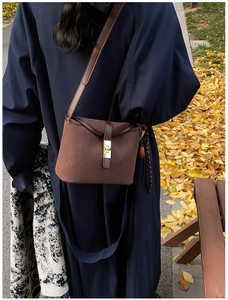 Detail of a brown suede bucket bag with gold clasp and braided drawstring outdoors