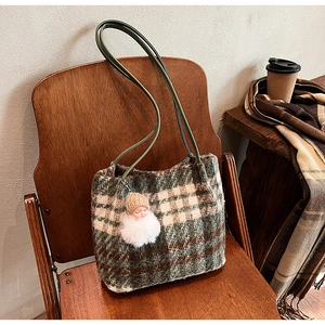 Détail du sac cabas en laine à carreaux avec pendentif poupée sur une chaise vintage