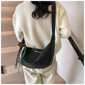 Detail view of black crescent moon bag featuring a woven rope charm and leather strap